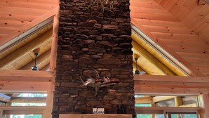 Ein Blockhaus-Interieur mit Kamin aus Stein, Holzbalken und einer Holzdiele mit einem Stuhl.