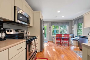 Une cuisine équipée d’une cuisinière, d’un four à micro-ondes et d’un four traditionnel, un coin repas avec une table et des chaises, et une vue sur la verdure environnante.