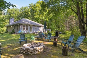 Une maison avec une cheminée, un foyer extérieur et plusieurs fauteuils Adirondack.