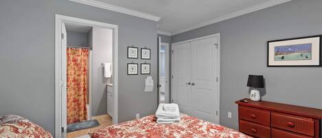 Een slaapkamer met een bed, een dressoir, een deur en een plafondventilator.