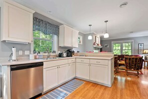 Une cuisine moderne avec des meubles blancs, un lave-vaisselle et un coin repas comprenant un canapé rouge et des chaises à motifs.