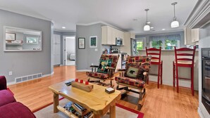 A living room with a wooden coffee table, red chairs, a fireplace, and a kitchen area with cabinets and a microwave. - Blue Bear Cottage: Serene Fish Creek Escape (Fish Creek)