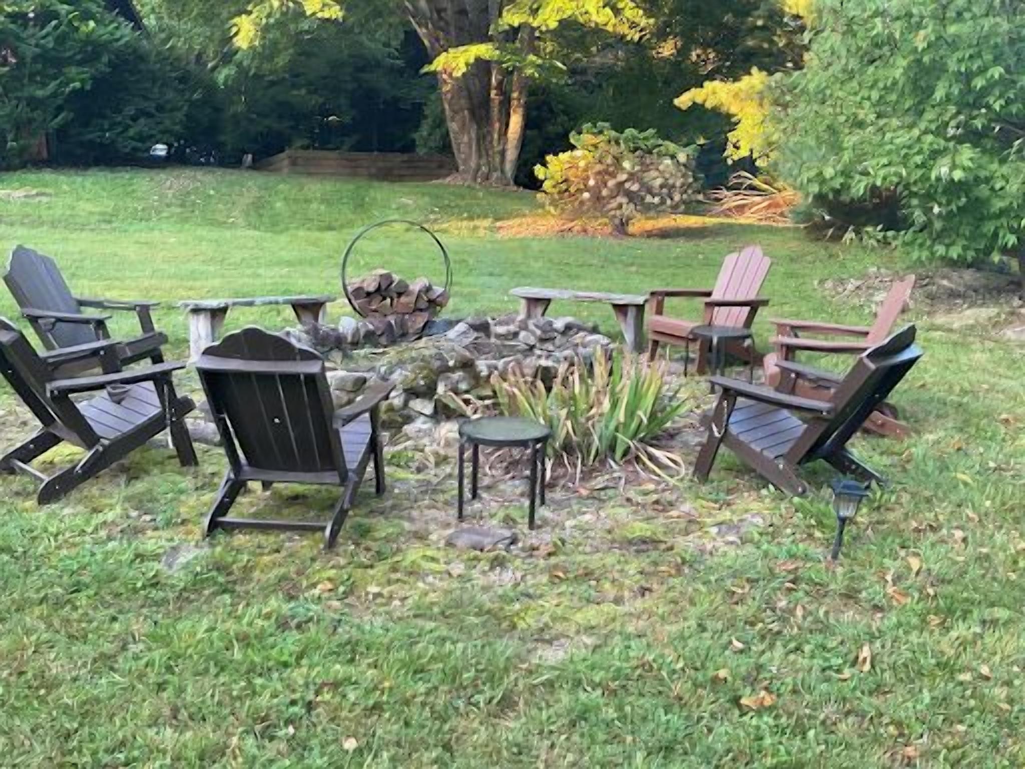 En utomhusplats med sittmöbler, inklusive Adirondack-stolar, och en eldstad.