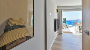 Une chambre d’hôtel moderne dotée d’un grand miroir, d’un téléviseur à écran plat fixé au mur et offrant une vue sur la piscine et l’espace extérieur aménagé.