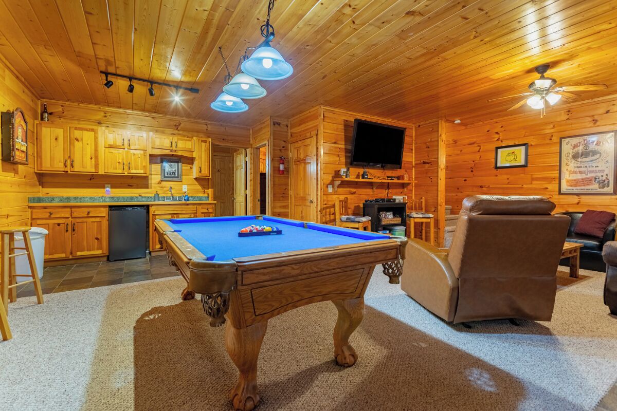 A wooden cabin interior with a pool table, a sofa, and a television.