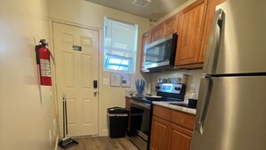 A compact kitchen with wooden cabinets, a stainless steel refrigerator, a microwave, and a stove. There is a fire extinguisher mounted on the wall near the door. - Chic 5-bedroom/ 2 B apartment in Washington with AC, WiFi (Washington)