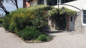 A house with a gravel driveway, a stone wall, and a garden with various plants and flowers. - La Vie en Rose Resort (San Vito al Tagliamento)