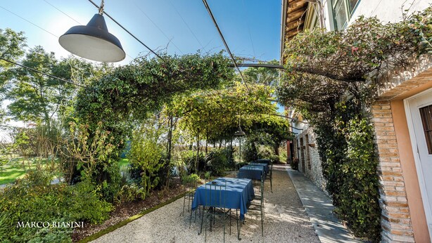 An outdoor patio with tables and chairs, surrounded by greenery and a brick wall. - La Vie en Rose Resort (San Vito al Tagliamento)