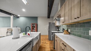 A modern kitchen with white countertops, wooden cabinets, a stainless steel refrigerator, and a wooden floor. - Modern Studio - Main St Penn Yan (Penn Yan)