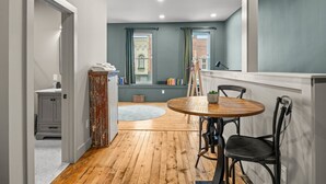 A room with a wooden floor, a round table with chairs, a window with curtains, and a view of a building outside. - Modern Studio - Main St Penn Yan (Penn Yan)