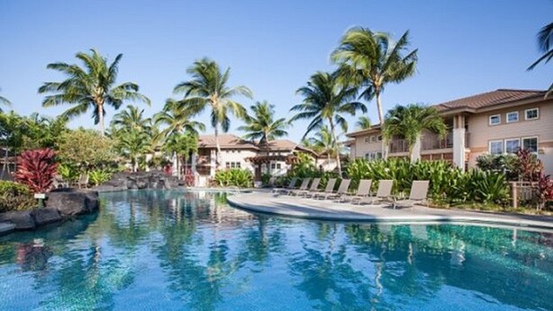 A swimming pool surrounded by palm trees and lounge chairs, with a building in the background. - Includes Beach Gear!  2404 Waikoloa Colony Villas (Waikoloa Beach Resort)