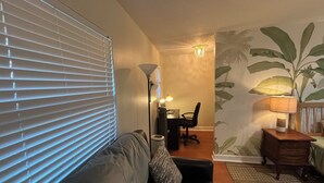 Een woonkamer met een bank, een bureau met een stoel, een lamp en een wand met een plantenmuur.