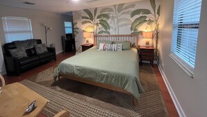 Een slaapkamer met een bed, nachtkastje, lamp, plafondventilator en een raam met jaloezieën.