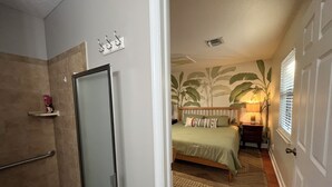Een slaapkamer met een bed, een nachtkastje, een wandplank en een deur naar een badkamer.