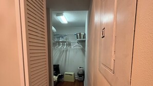 Een smalle gang met een houten vloer die leidt naar een kamer met een bed, een kleine tafel en een kast met hangende kleding.