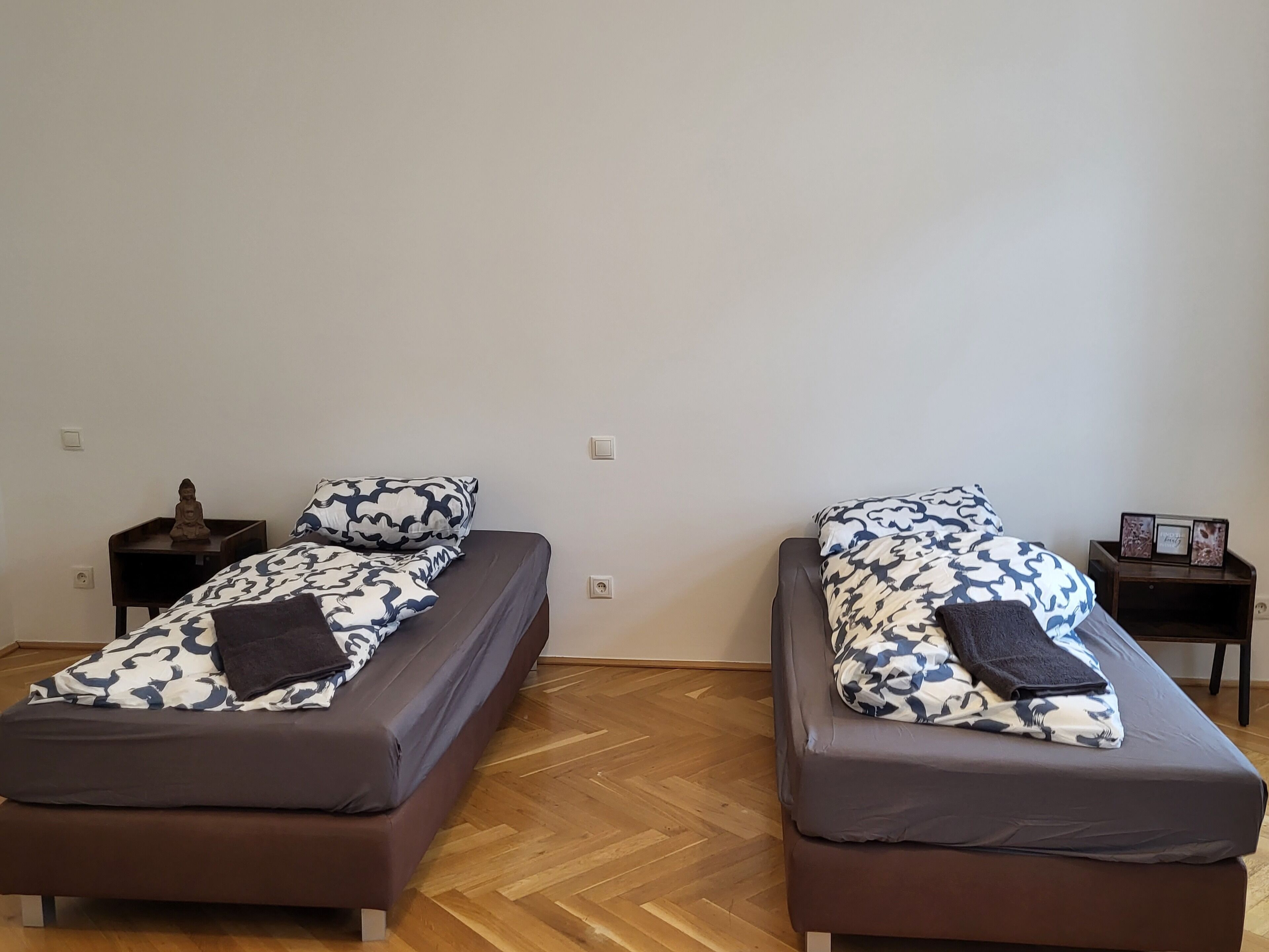 Twee eenpersoonsbedden met behang, houten nachtkastjes en een visgraatvloer.