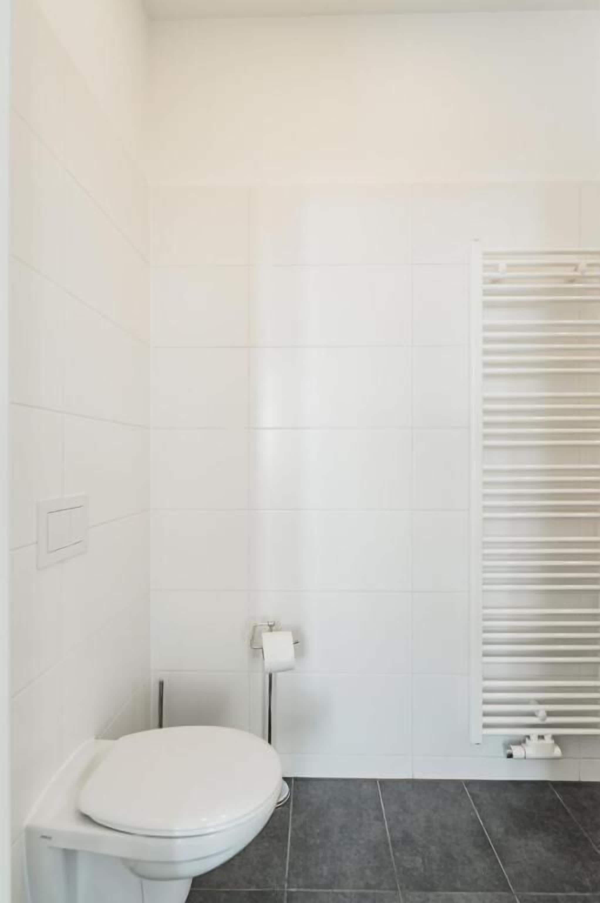 A bathroom with white tiles, a white toilet, and a towel rack.