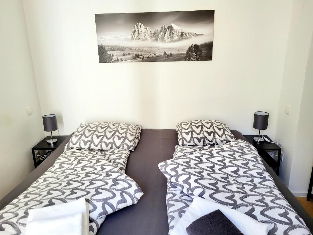 Ein Doppelbett mit gemusterten Betttextilien, zwei Nachttische mit Lampen und ein gerahmtes Landschaftsfoto an der Wand.