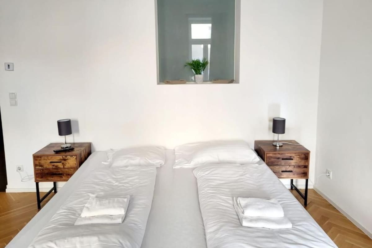 A bedroom with two beds, a mirror above the beds, and a window.