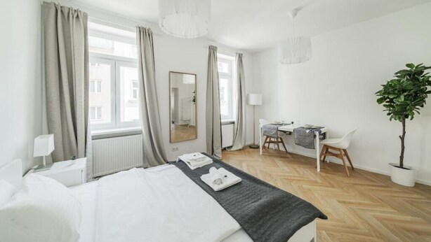 Una habitación de hotel con cama, escritorio, silla, espejo y planta en maceta.