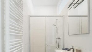 Un baño moderno con cabina de ducha de vidrio, muebles blancos y un espejo grande.