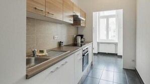 Una cocina moderna con armarios blancos, piso de baldosas oscuras y ventana que deja entrar luz natural.