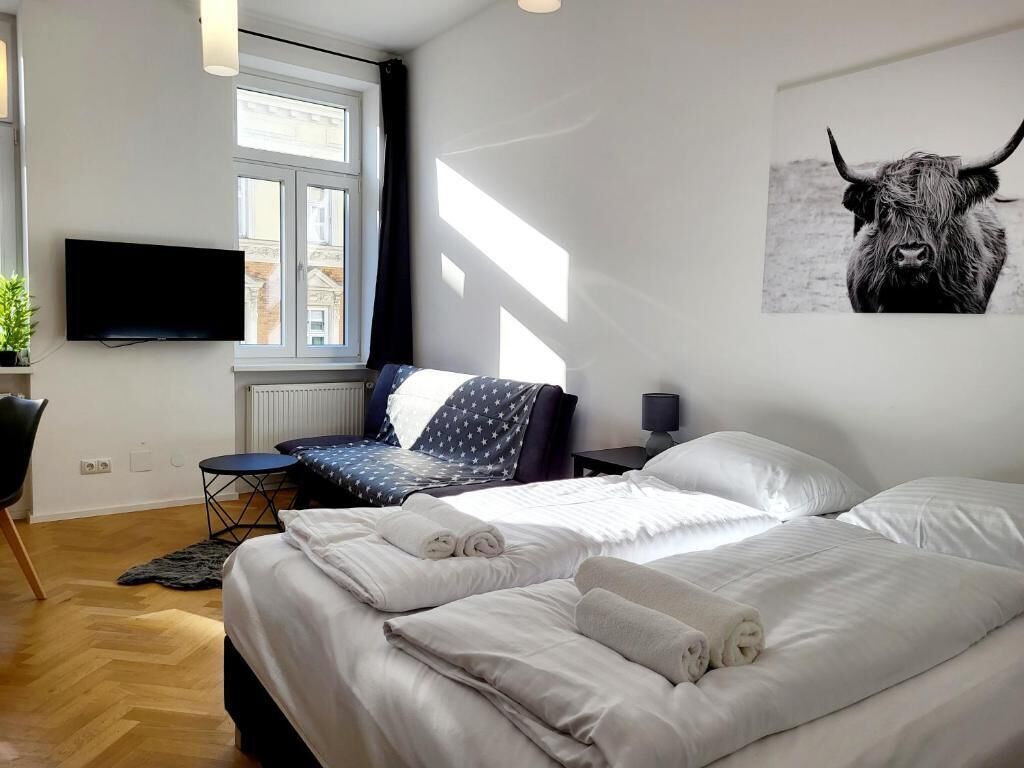 Una habitación de hotel moderna con una cama grande, un televisor de pantalla plana, una ventana con persianas, una mesita pequeña y una silla.