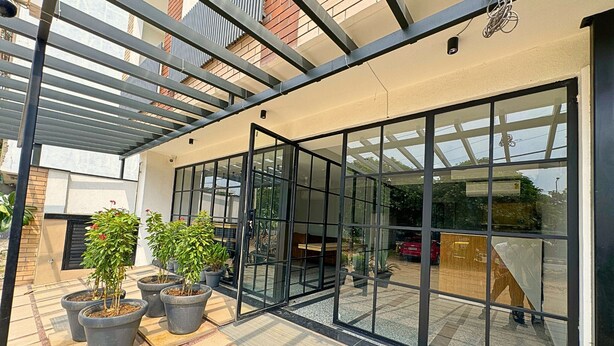 A modern building with large glass doors, potted plants, and a tiled patio area. - Lime Tree Hotel Sector 51 Gurgaon (Gurugram)