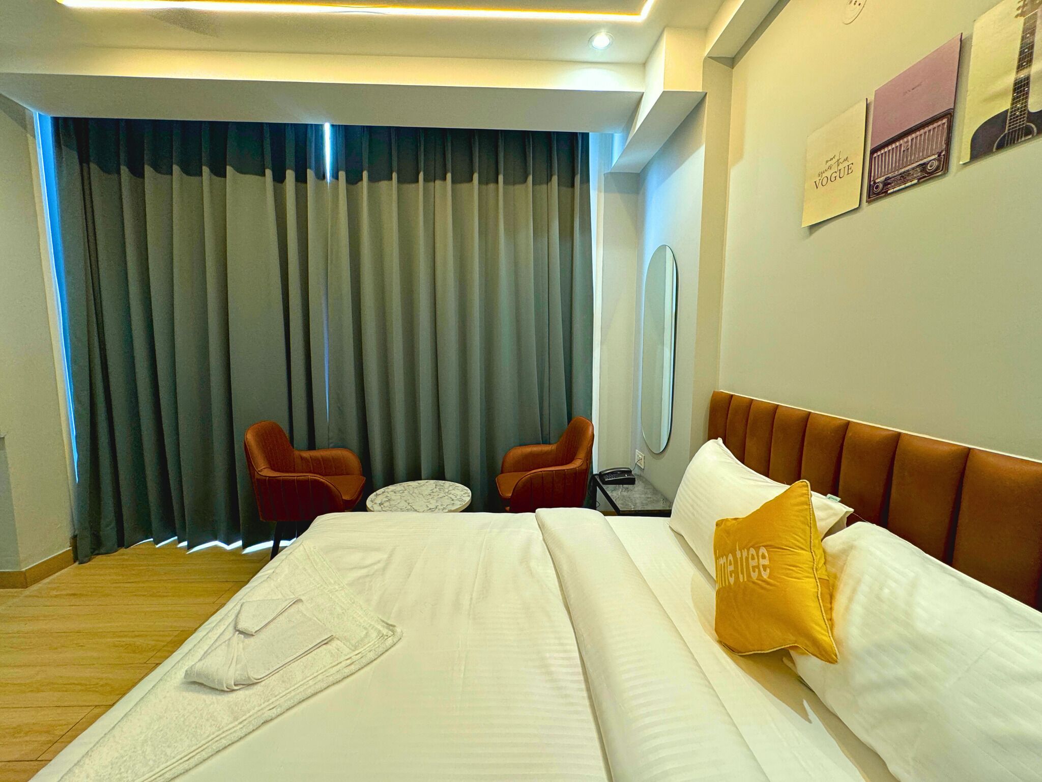 Habitación de hotel con una cama, dos sillas, una mesita, un espejo y una ventana con cortinas.