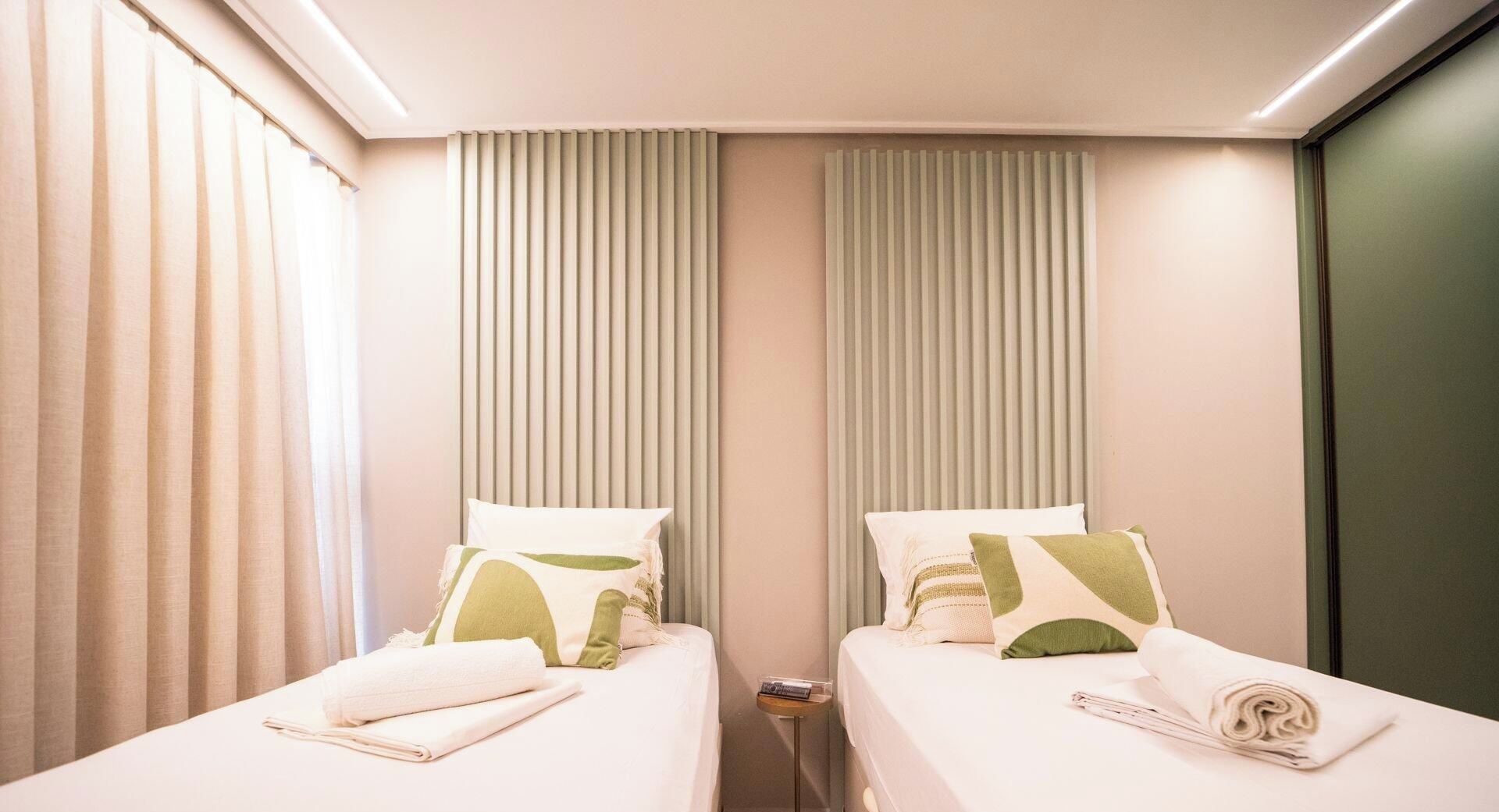 Una habitación de hotel con dos camas, cada una con una almohada y una toalla enrollada.