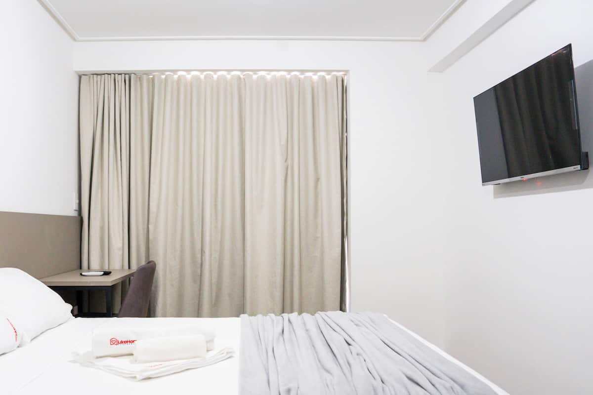 A hotel room with a bed, a desk, a chair, a TV, and a window with curtains.