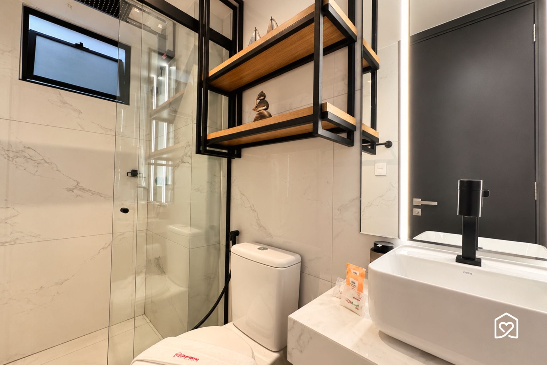 Un baño moderno con cabina de ducha de vidrio, inodoro y lavamanos con espejo. Hay repisas de madera sobre el inodoro y un grifo negro en el lavamanos.
