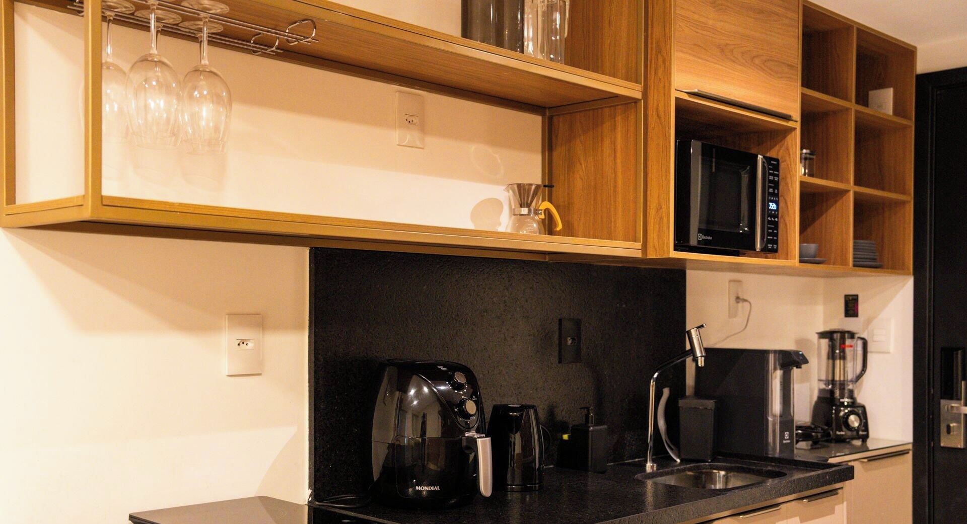 A kitchen with a black countertop, a coffee maker, a kettle, a microwave, and a wine rack.