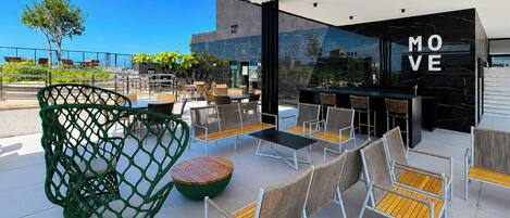 An outdoor seating area with chairs and tables, a bar area with a 'MOVE' sign, and a view of the cityscape.