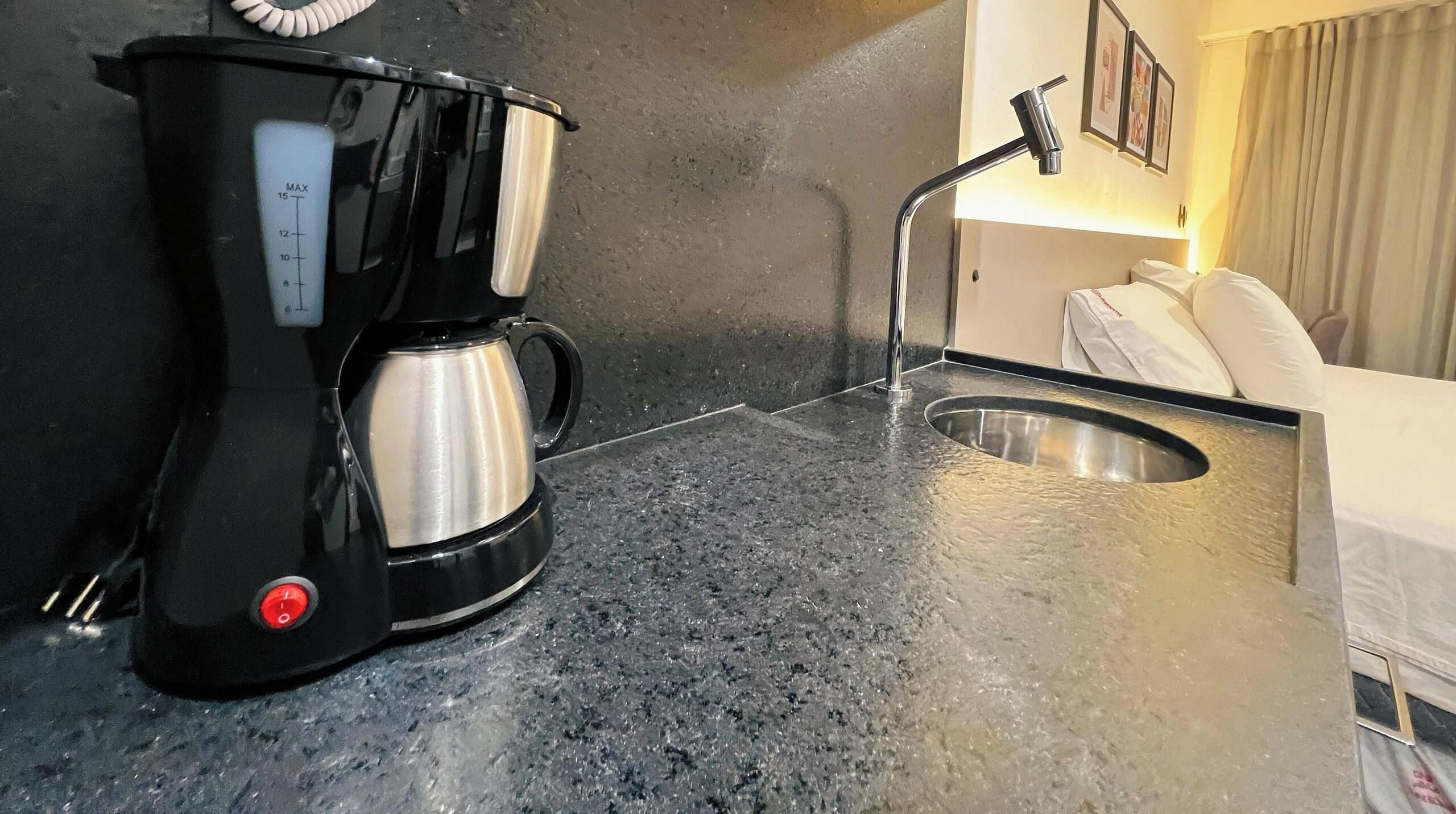 Uma cozinha compacta com cafeteira, pia e torneira.