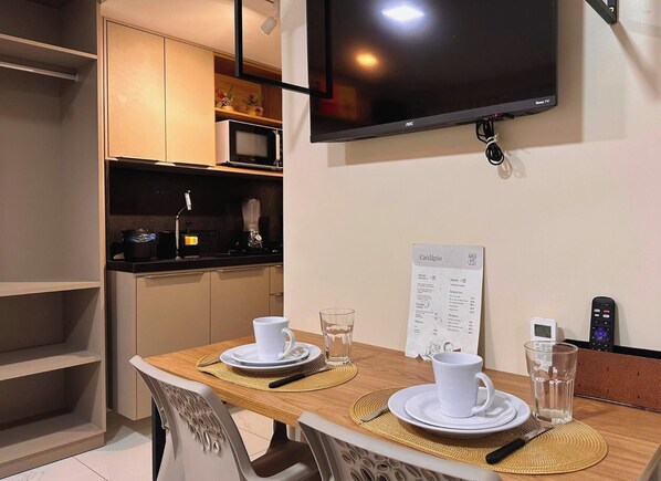 A compact kitchen with a microwave, coffee machine, and a TV mounted on the wall. - Move Tambaú (João Pessoa)