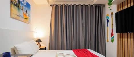 Ein Hotelzimmer mit einem Bett, einem Gemälde, einem Vorhang, einem Fernseher und einer Pflanze.