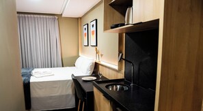 A compact hotel room with a bed, a small kitchenette, and a window with curtains. - Move Tambaú (João Pessoa)