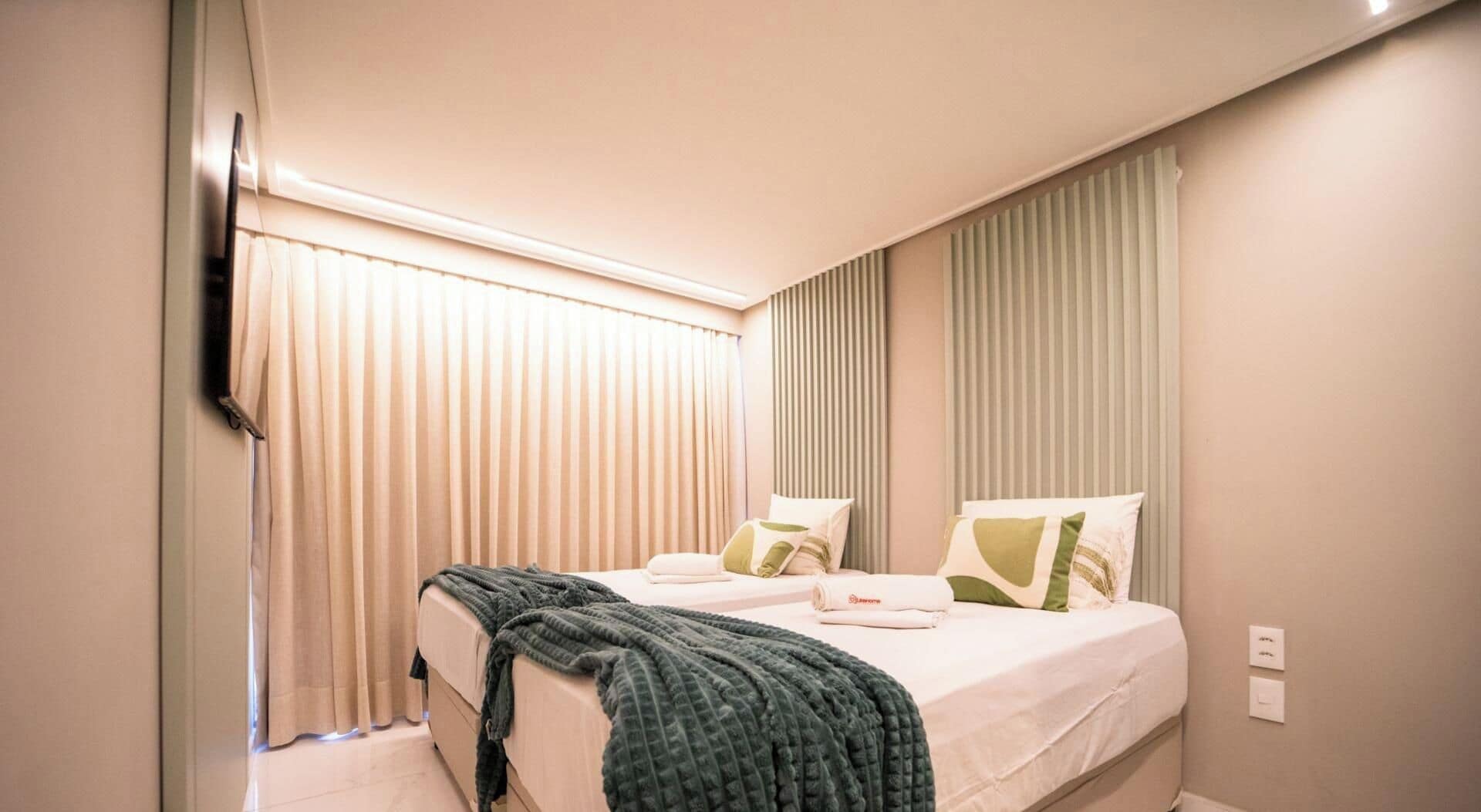 A hotel room with a bed, two pillows, a blanket, and a window with curtains.