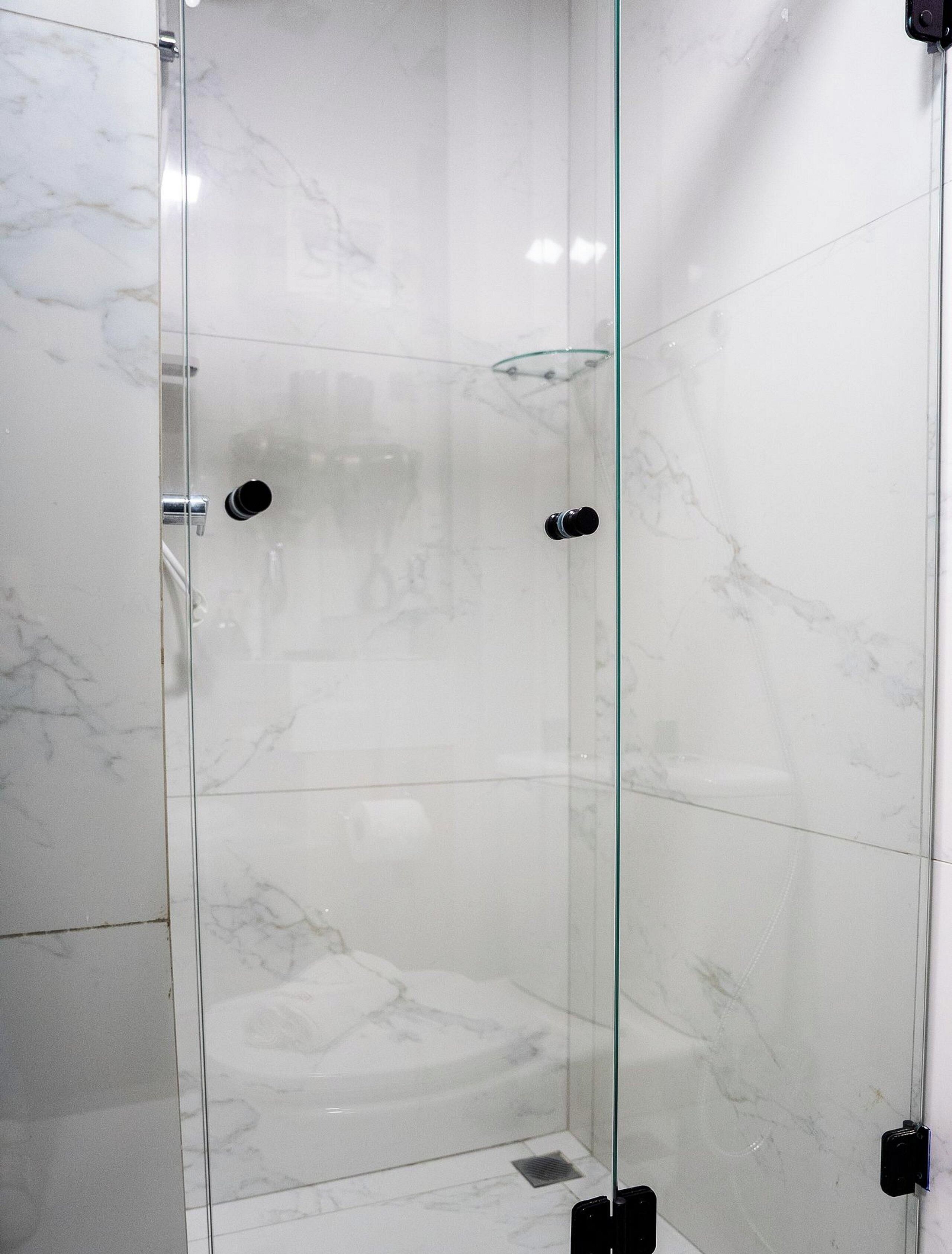 Un vestuario de ducha con paredes de vidrio, suelo de mármol y puerta de cristal.