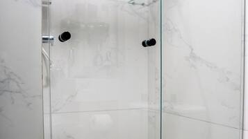 Un vestuario de ducha con paredes de vidrio, suelo de mármol y puerta de cristal.