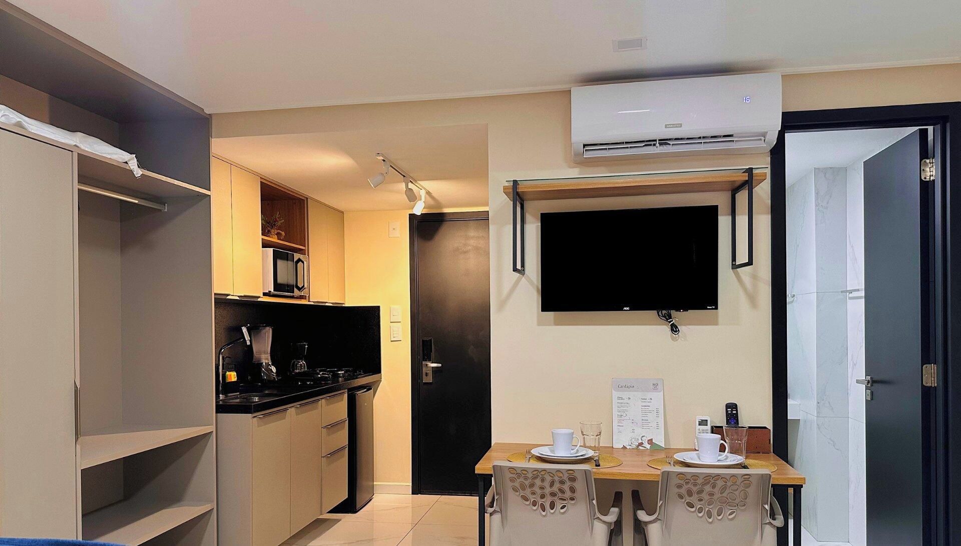 Cozinha compacta com micro-ondas, fogão e TV de tela plana presa na parede.