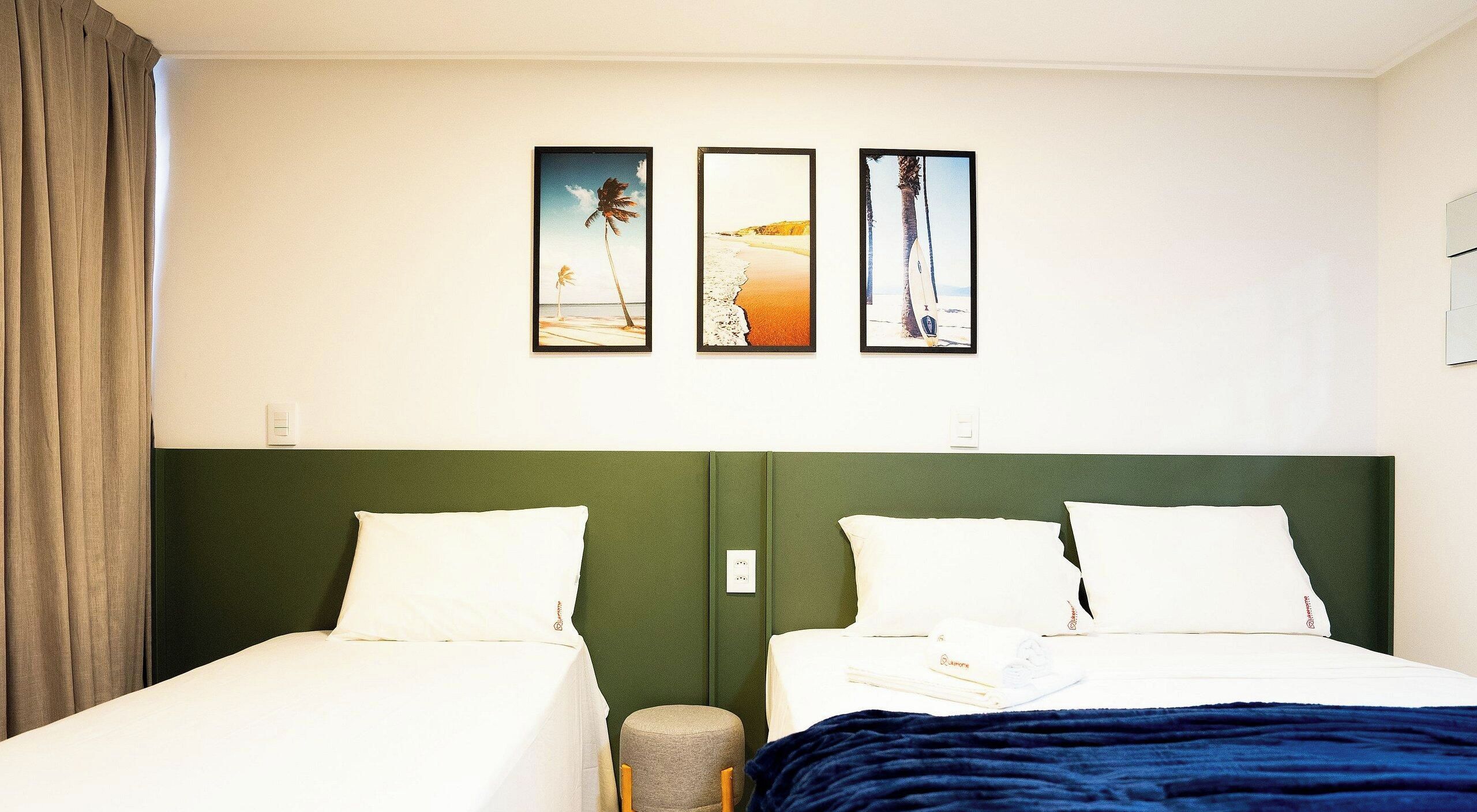 A hotel room with two beds, a green headboard, and three framed pictures on the wall.