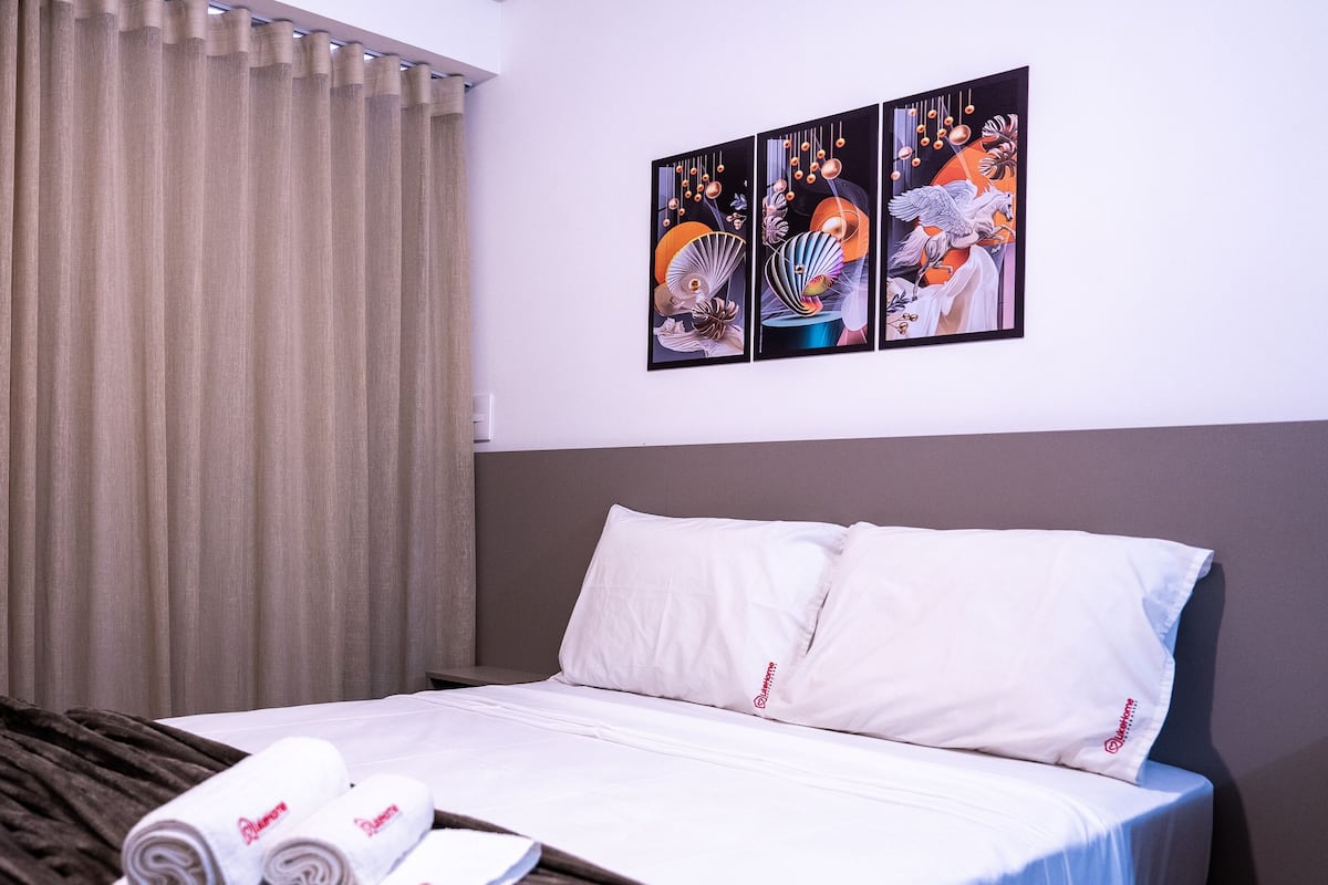 A hotel room with a bed, white pillows, a rolled-up towel, and a set of curtains.