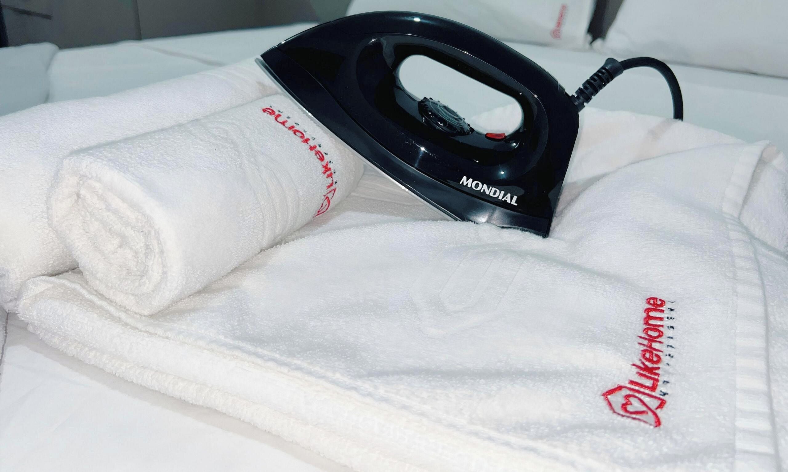 A neatly folded white towel with embroidered text and a black iron placed on top.