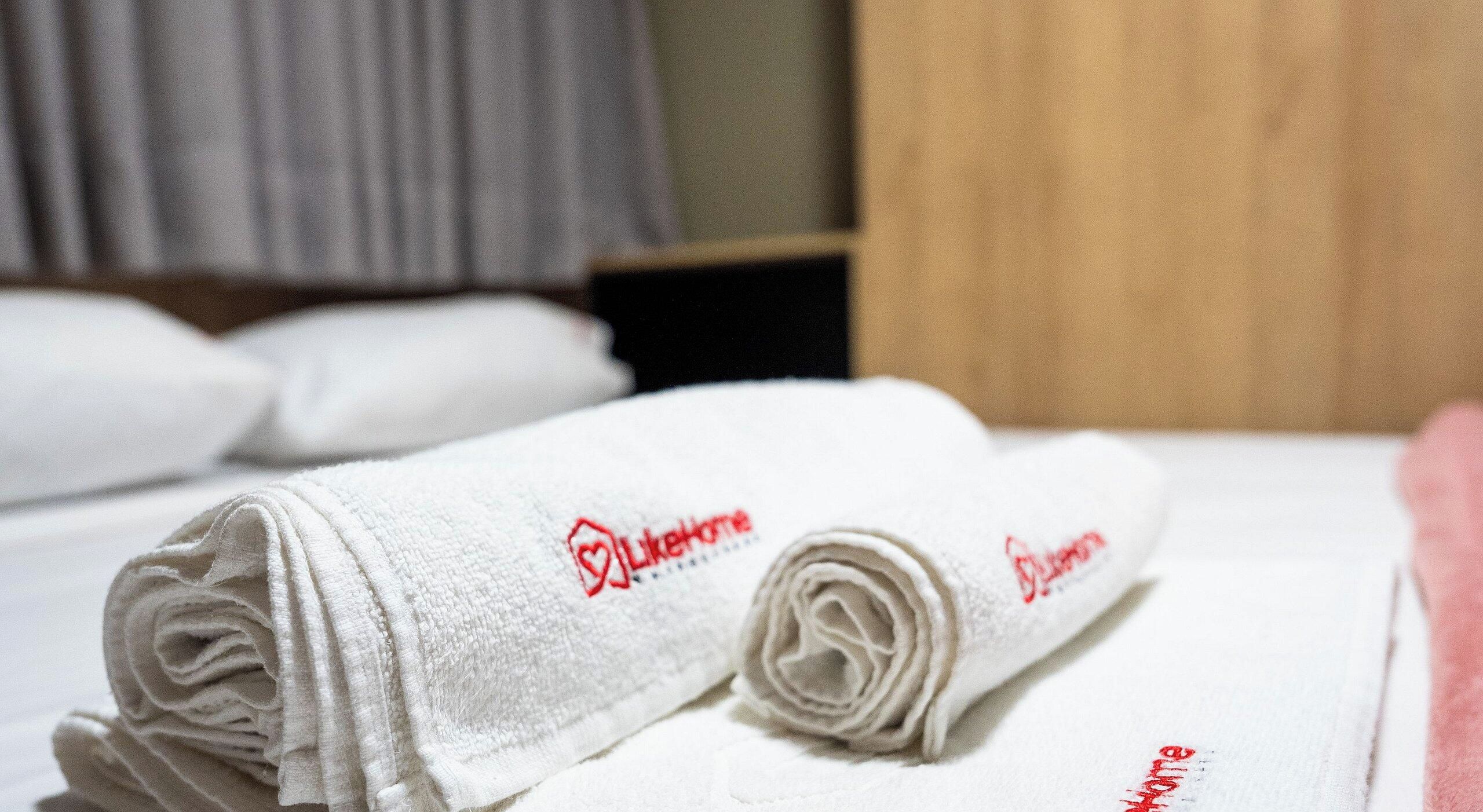Una cama bien hecha con toallas blancas enrolladas y una manta rosa.