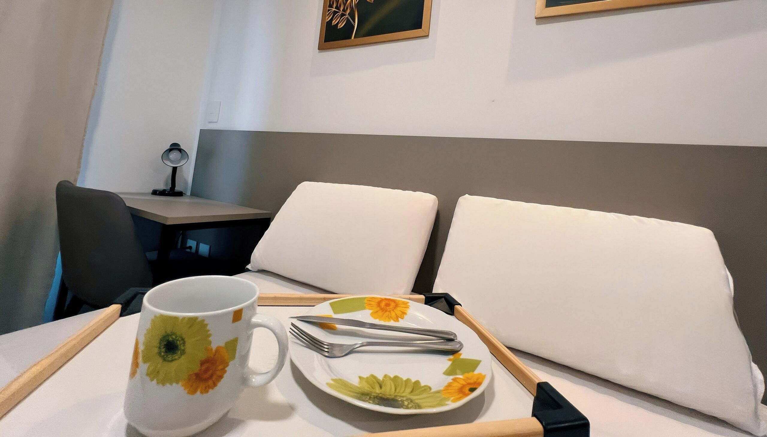 A hotel room with a dining table set for two, a coffee mug, and a plate with cutlery.