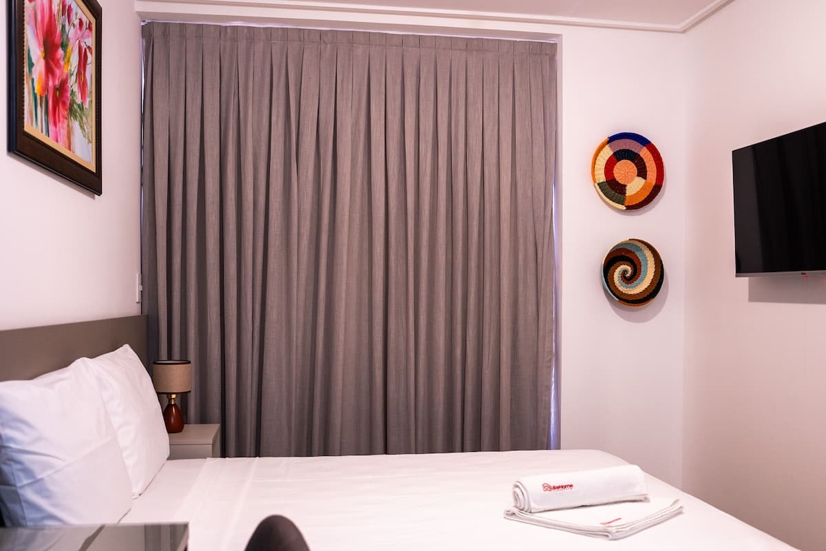 A hotel room with a bed, a TV, a window with curtains, and a wall with two decorative plates.
