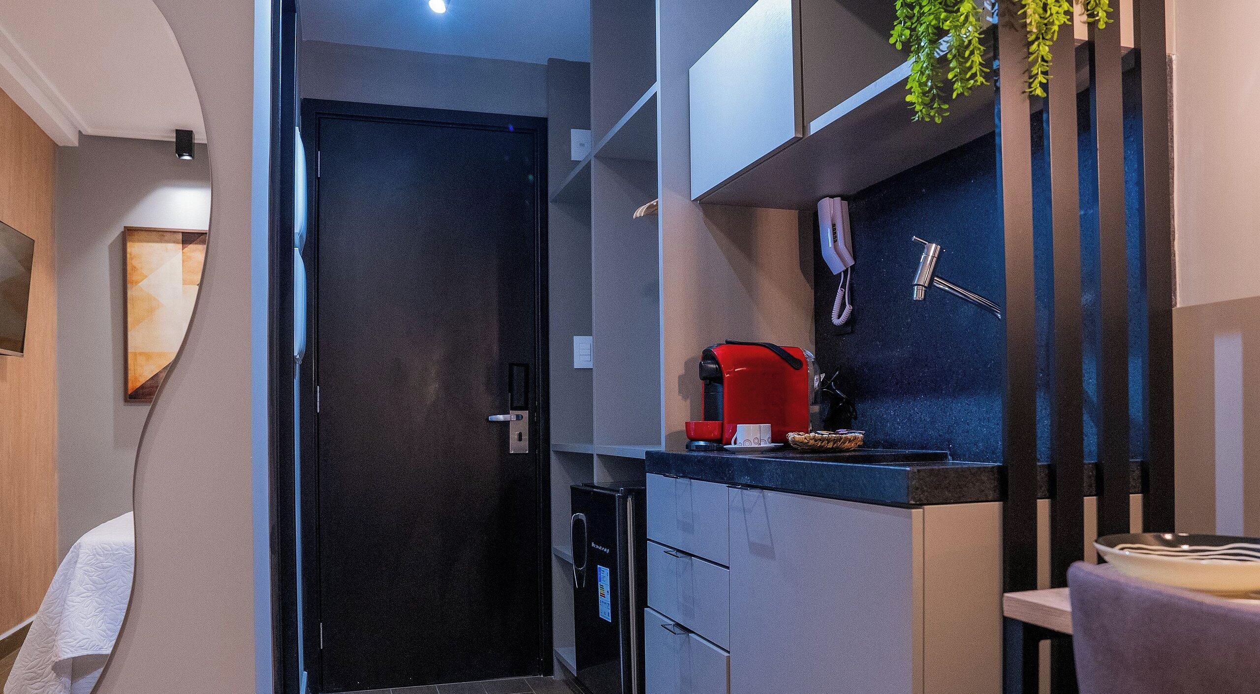 Una cocina moderna con un refrigerador negro, una cafetera roja y un pequeño comedor con una mesa y sillas.