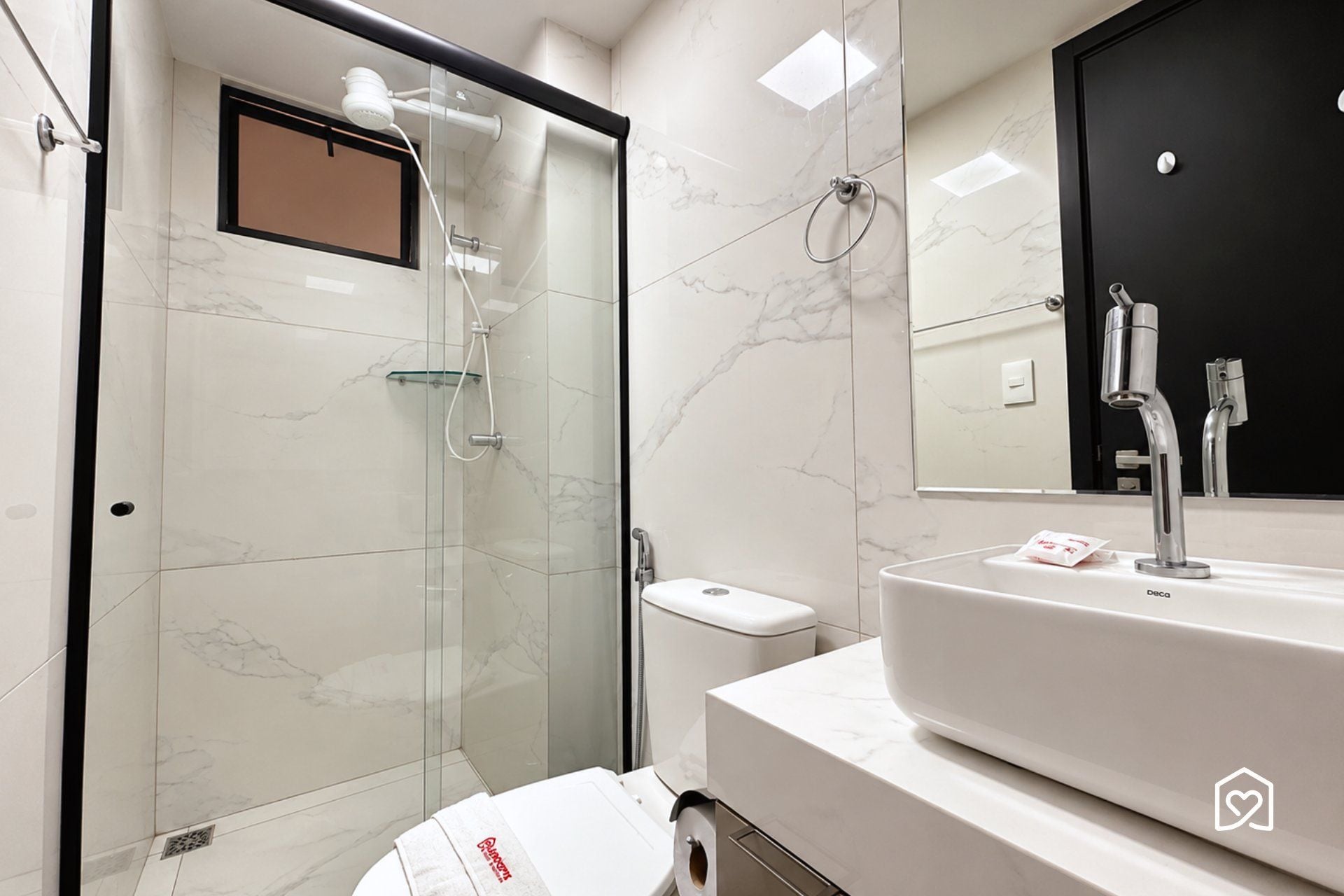 A modern bathroom with a glass-enclosed shower, a white sink, and a black-framed mirror.